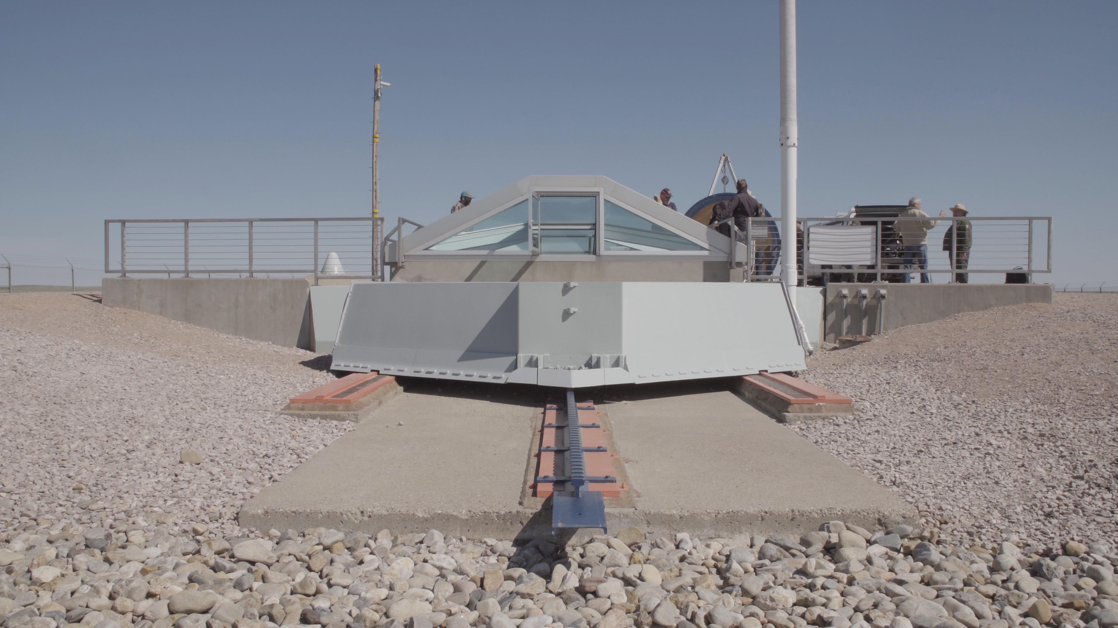 Visitors stand above a decommissioned missile launch facility in a sparse western landscape.
