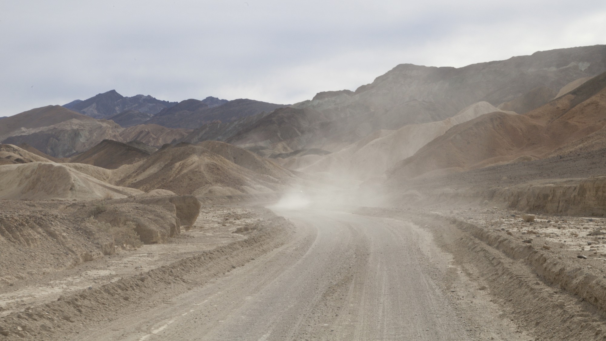 A dusty unpaved road curves through layered desert hills in Death Valley.