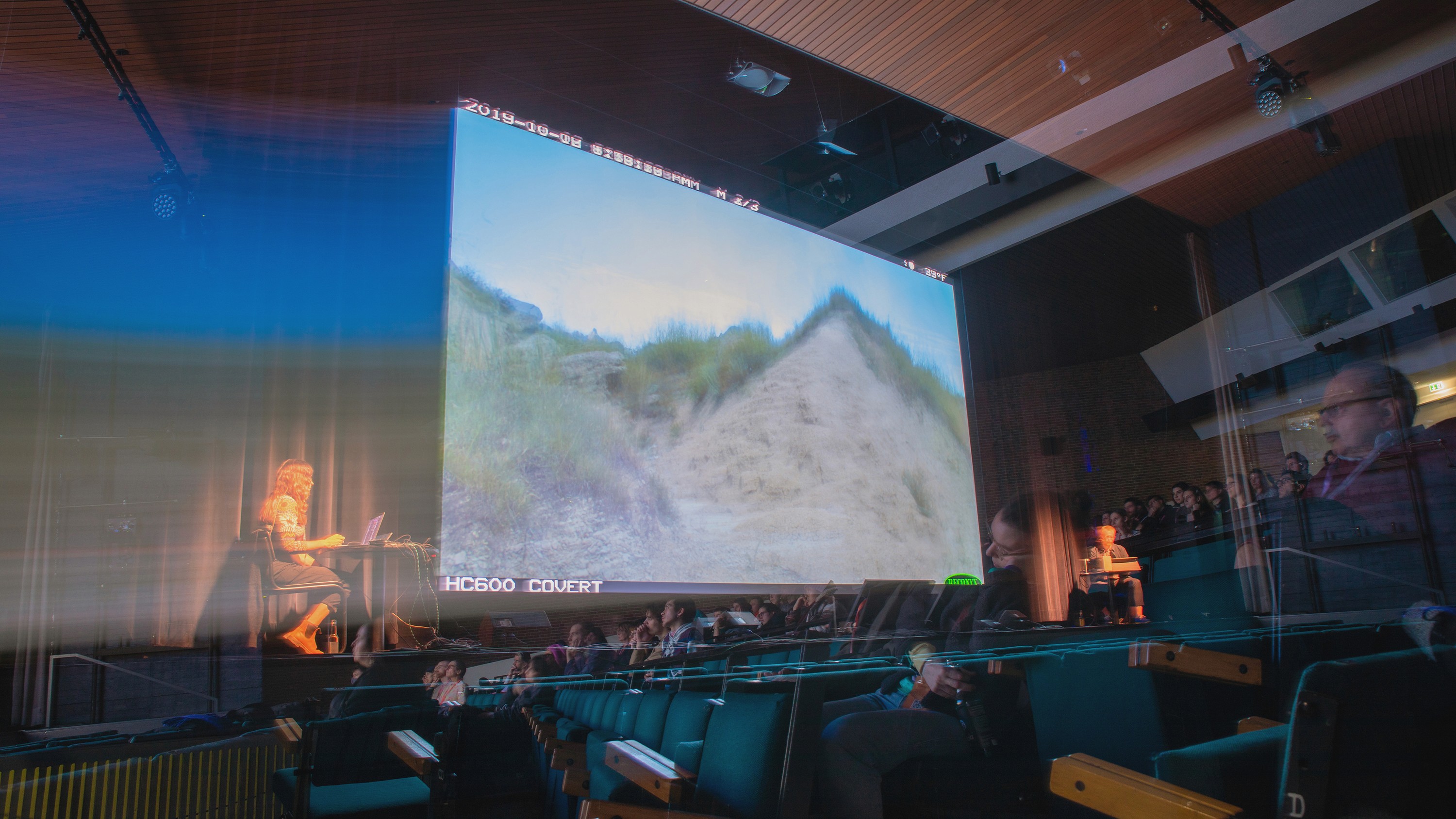 Performers flank a large screen displaying a virtual Badlands landscape in an auditorium.