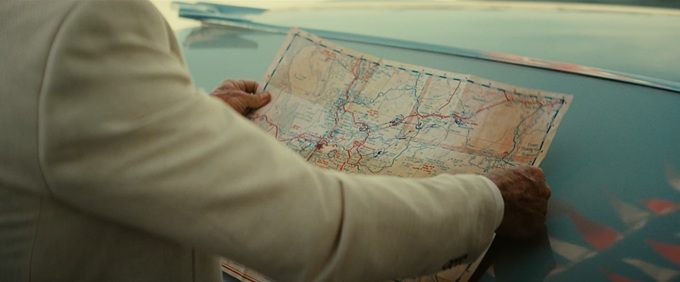 Hands holding a marked road map across the hood of a car.
