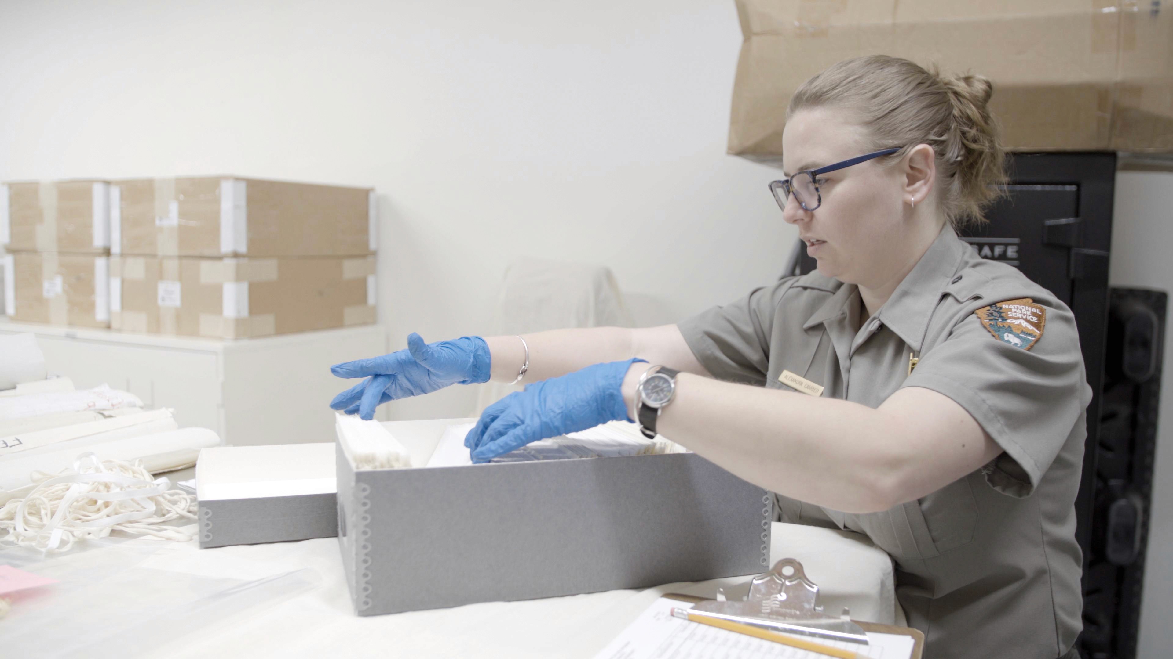 A National Park Service staff member works with labeled specimens and archival containers at a collections table.