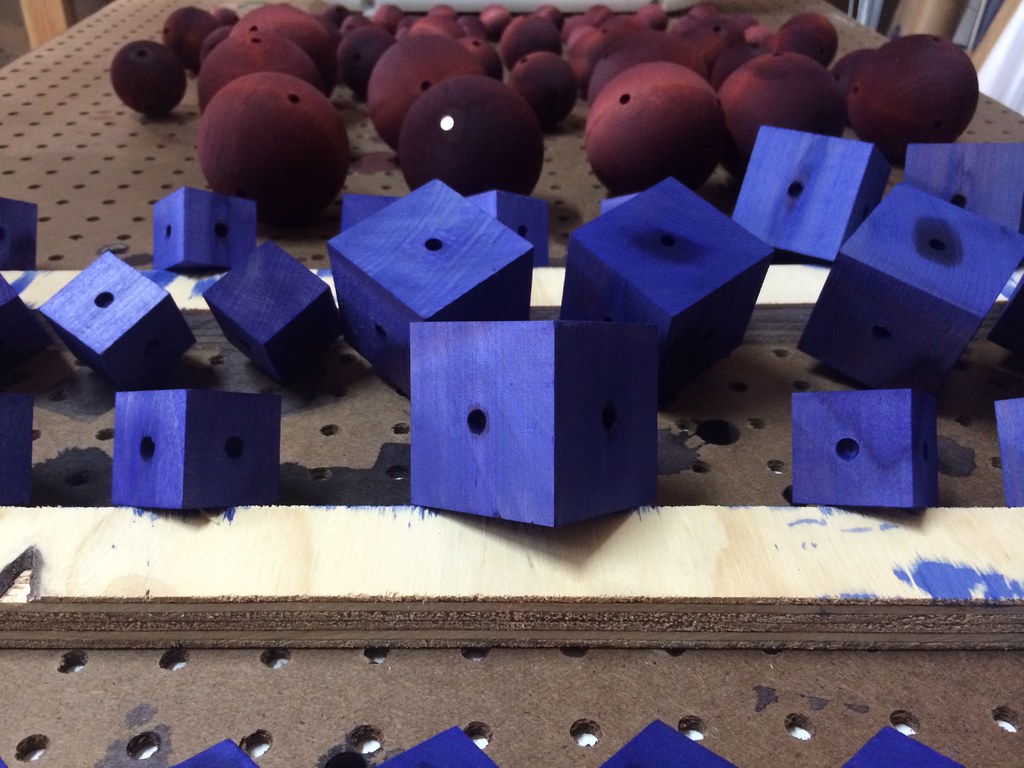 Rows of blue-purple wooden cubes and reddish wooden spheres dry after staining for the Curio Aquarium modular toys.