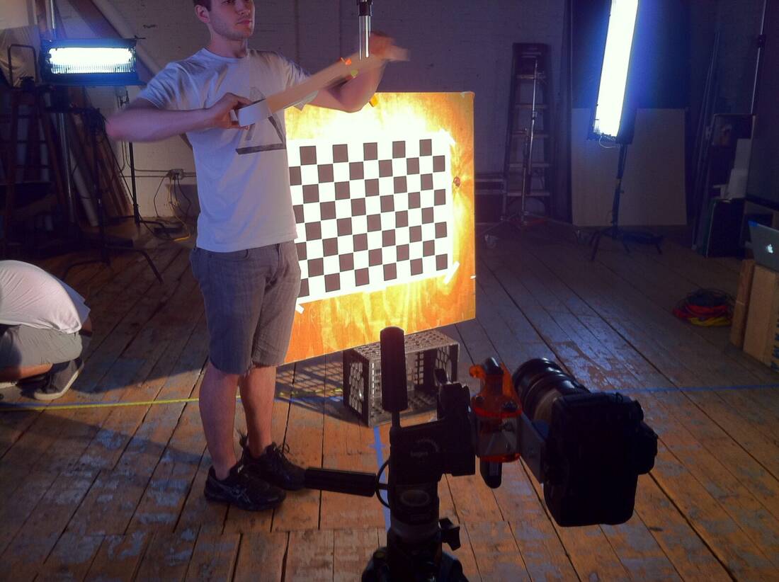 A checkerboard target is held in front of one RGB-D rig during the four-camera Stüssy capture.