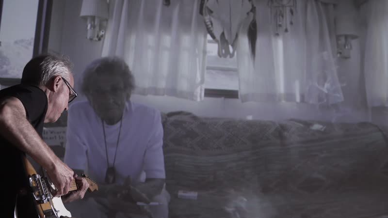 Composer Bill Frisell plays guitar at the left of the frame while footage from Truth or Consequences is projected across the wall behind him.
