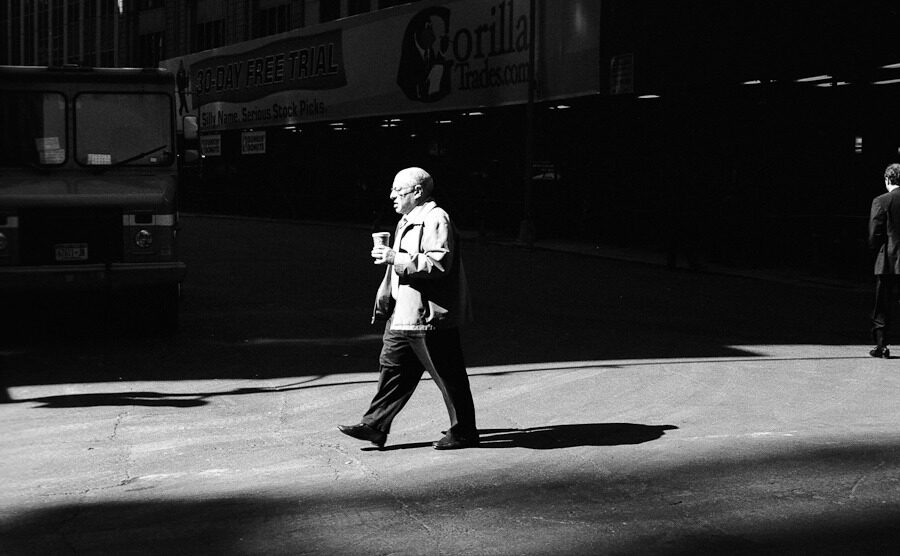 Sunlit pedestrian crossing a dark city street in black and white.