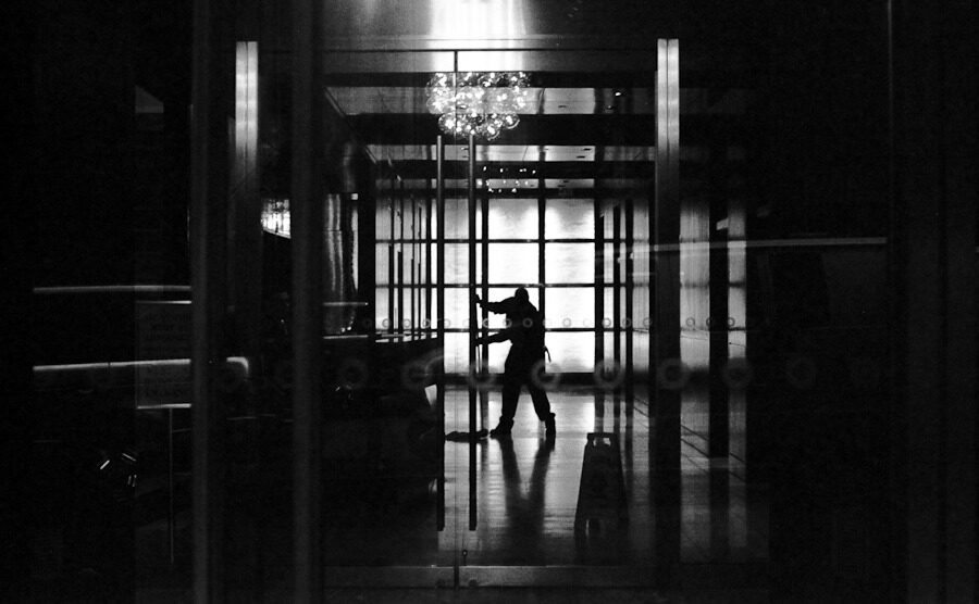 Silhouetted person walking through the glass doors of a dark lobby.