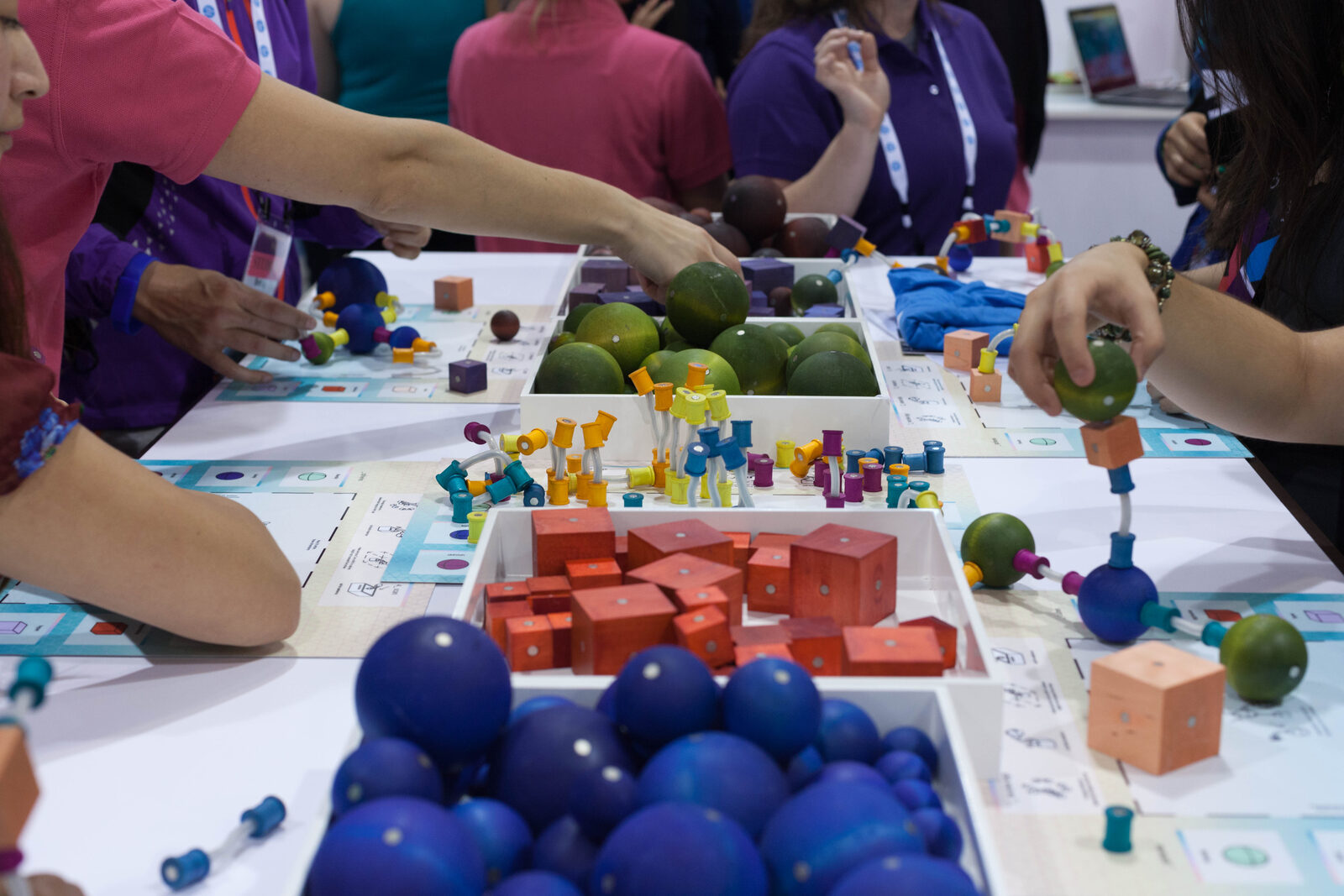 Participants assemble colorful modular creatures around a table filled with geometric parts and fruit.