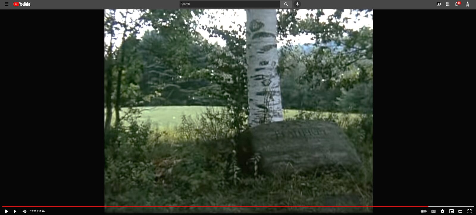 The carved R. Flaherty grave stone beside a birch tree in present-day footage of the farm.