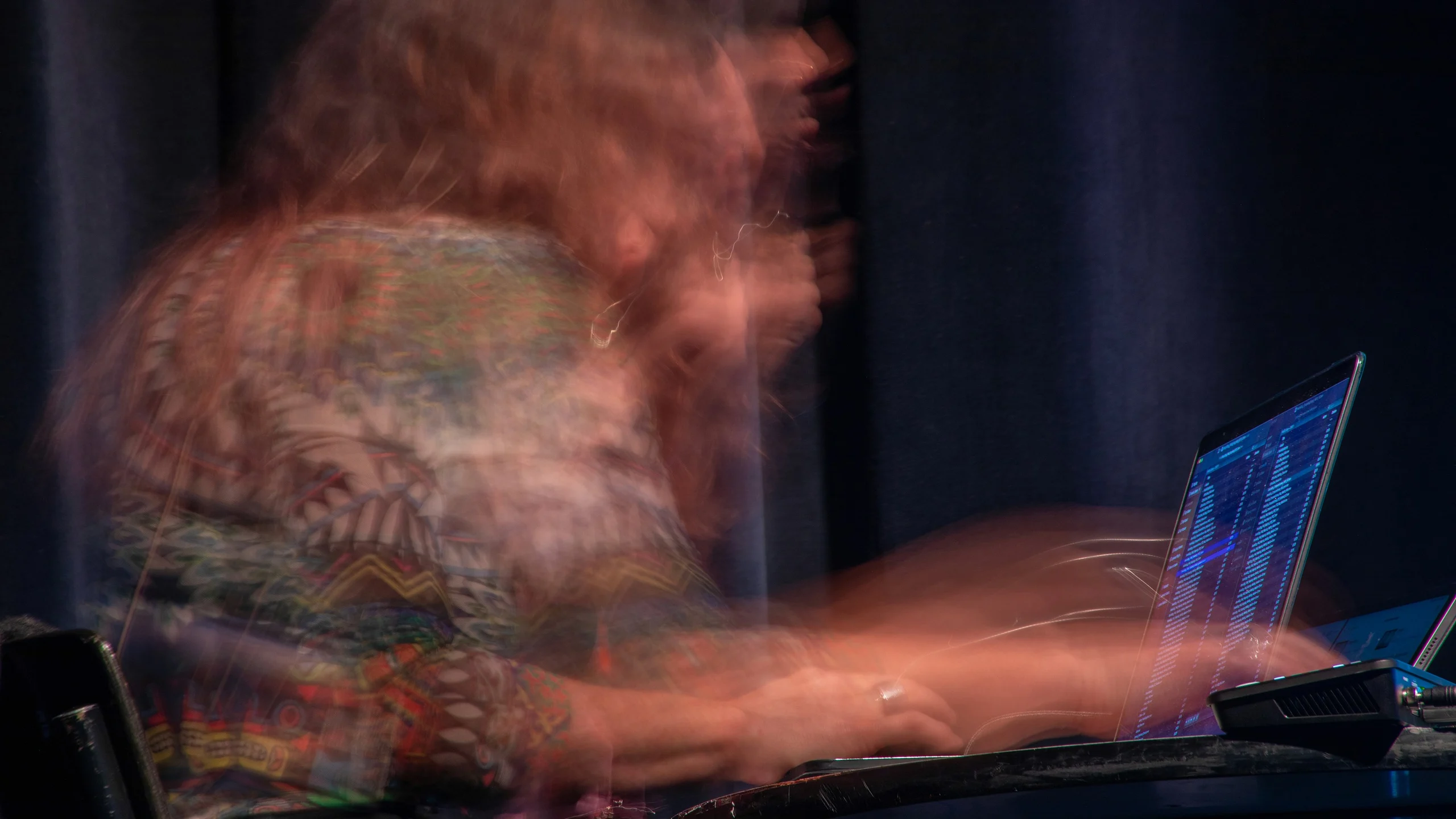 A motion-blurred performer works at a laptop as a translucent volumetric landscape fills the stage behind them.