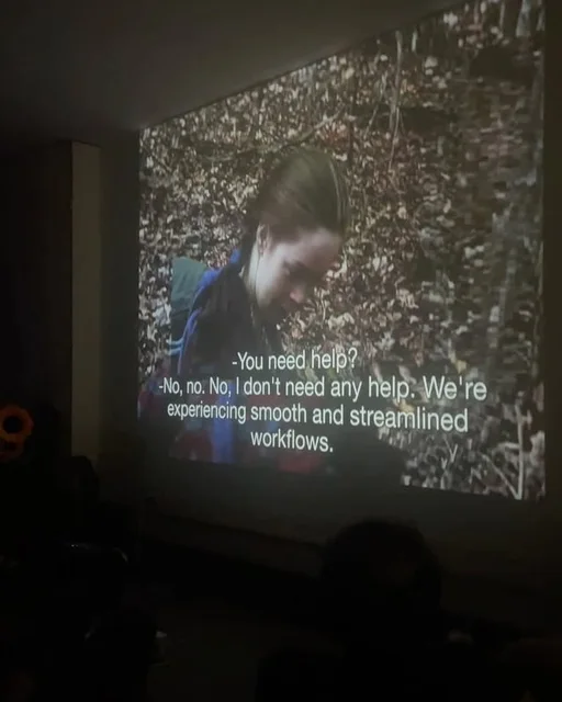 A Brooklyn screening of Smooth Blair Witch projected on a wall at LARPA; the stabilized forest image carries subtitles reading, ‘We’re experiencing smooth and streamlined workflows.’